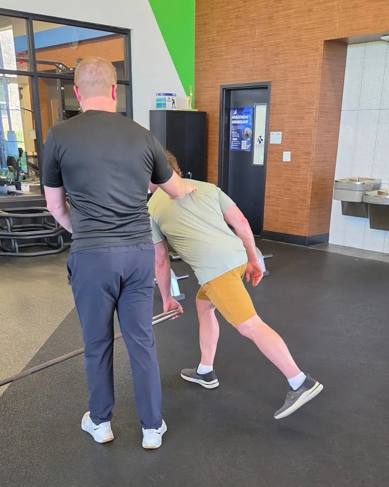 A Physio+ clinician cueing a patient through a single leg Romanian deadlift on a landmine bar